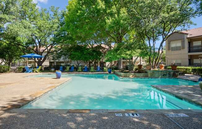 A swimming pool surrounded by trees and green and blue chairs at La Costa in Plano, TX.