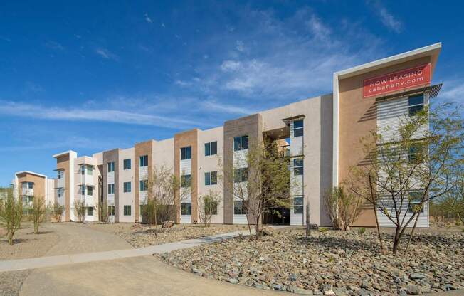 A building with a red sign that says "Now Leasing" is surrounded by rocks and trees.