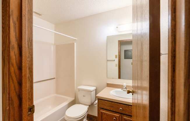 A bathroom with a toilet sink and tub and a mirror. Fargo, ND Huntington Apartments.