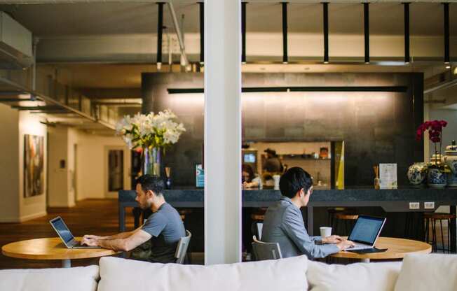 two men sitting at tables working on their laptops in a large open space