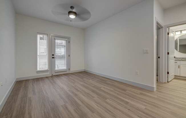 a living room with white walls and wood flooring and a door to a kitchen