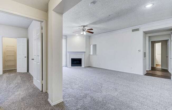 A spacious living room at Saxony at Chase Oaks Apartments in Dallas, TX, with carpeted flooring, a ceiling fan, a fireplace, and large sliding glass doors leading to a balcony.