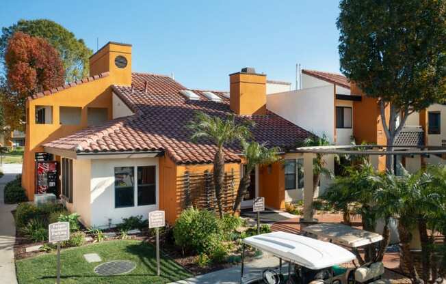 A yellow house with a red tile roof and a white surfboard leaning against it.