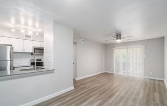 an empty living room with a kitchen in the background