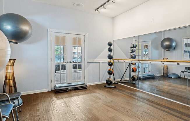 A room with a mirror, exercise balls, and a wooden floor.
