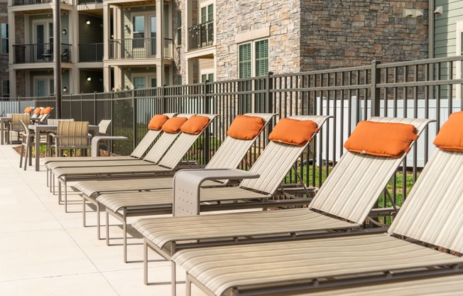 a row of lounge chairs with orange pillows in front of an apartment building at The Whitworth, Williamsburg, 23185