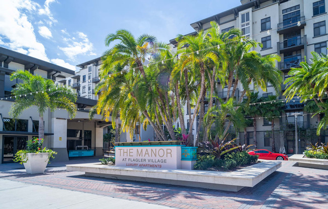 Monument sign in front of palm trees and mid-rise apartment building
