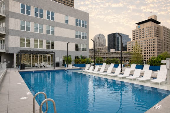 A large swimming pool with white chairs and a building in the background.
