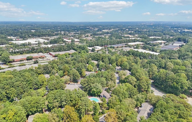 A bird's eye view of a forested area with a swimming pool and buildings in the distance.