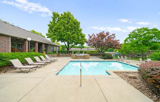 A pool surrounded by trees and chairs in front of a house.