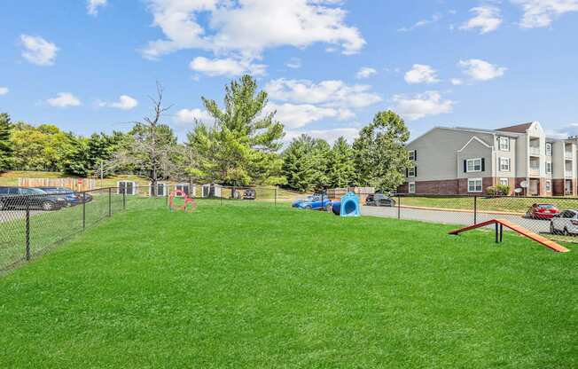 A grassy field with a playground and apartment building in the background.