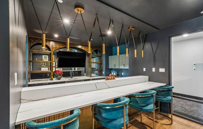 A modern kitchen with a long white counter and blue chairs.