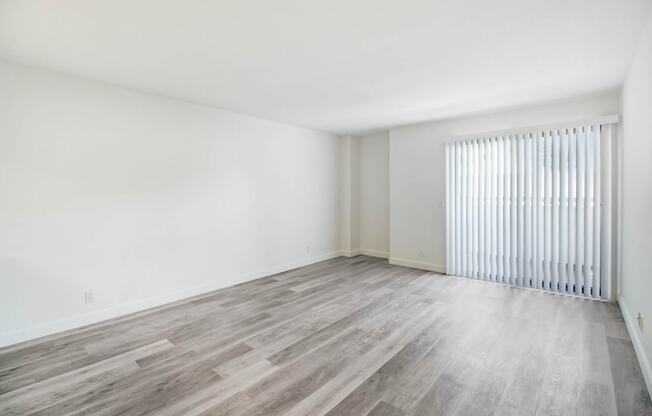 the living room of an apartment with wood flooring and a large window