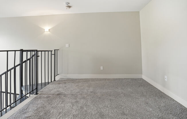 A spacious room with a carpeted floor and a staircase with black railings.