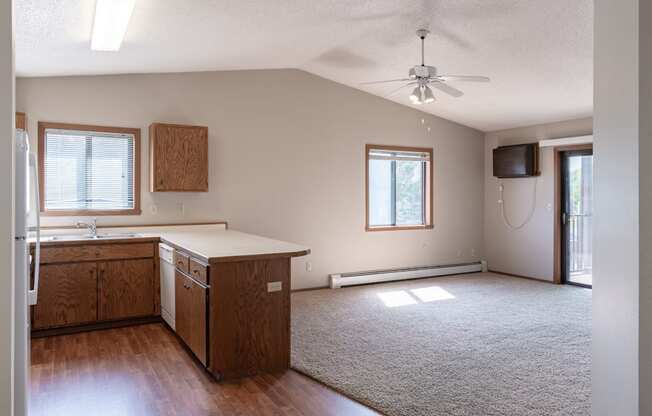 an empty living room with a kitchen and a ceiling fan. Fargo, ND Rosegate Apartments