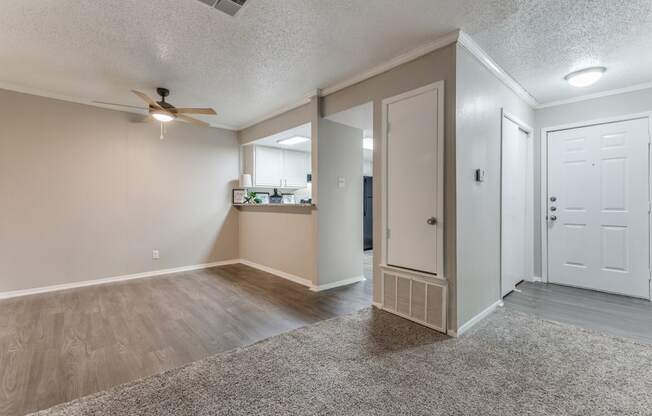 an empty living room with a ceiling fan and a kitchen in the background