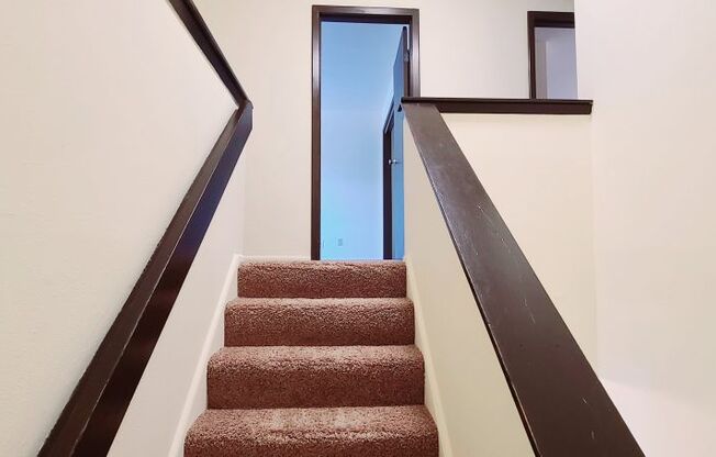 A staircase with a brown carpeted runner and dark wooden balusters.