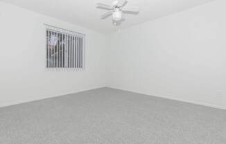 A room with a ceiling fan and a window with bars.