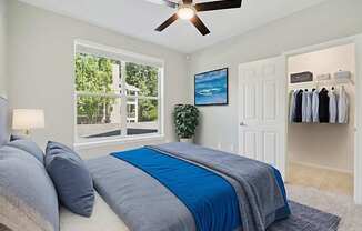 A bedroom with a bed, a ceiling fan, and a window with a view of a tree-filled outdoor area.