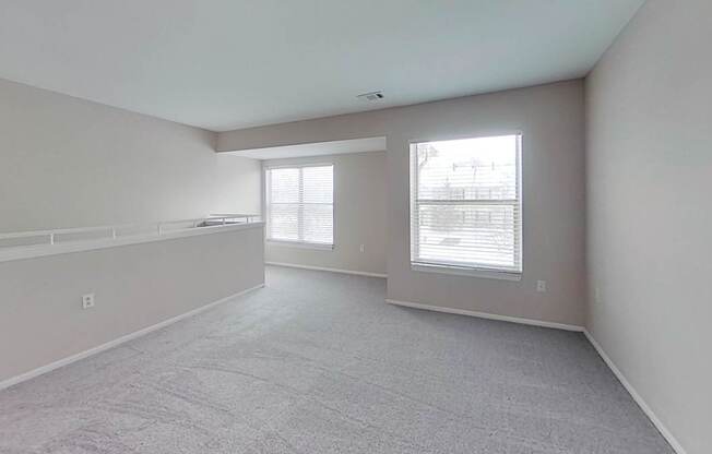 A spacious room with carpeted flooring and two large windows.
