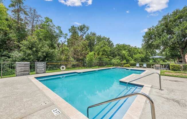 A swimming pool surrounded by trees and a clear blue sky.