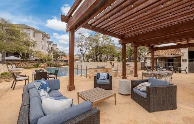 A patio with a wooden pergola and furniture including a couch and chairs.