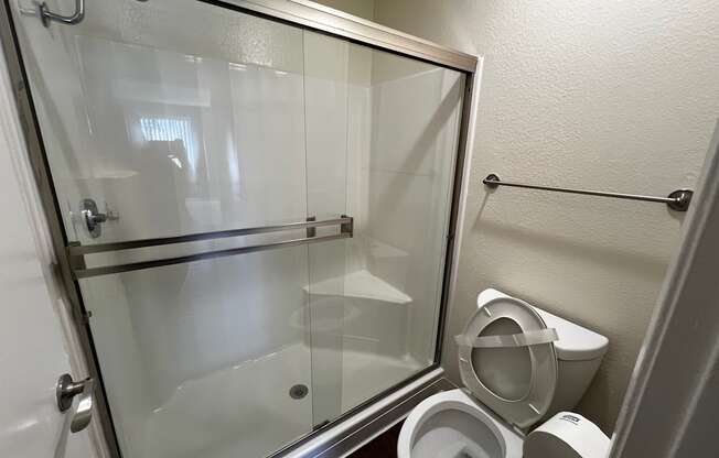 A white toilet sits next to a toilet paper roll in a small bathroom.
