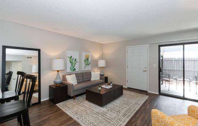 Apartments for Rent in Riverside, CA - Veranda Riverside - Living Room with Wood-Style Floor, Area Rug, Couch, Coffee Table, Side Tables with Lamps, Mirror, and Sliding Glass Door with Access to Private Patio