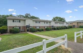 A white picket fence separates a grassy area from a row of houses.