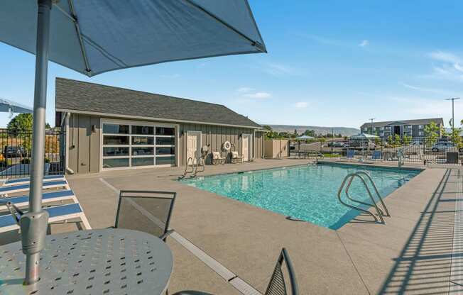 Bright blue pool with lounge chairs, umbrella-covered seating, and a view of the clubhouse. at Altitude, East Wenatchee, WA, 98802