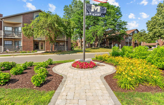 A garden with a flag pole in front of apartment buildings.