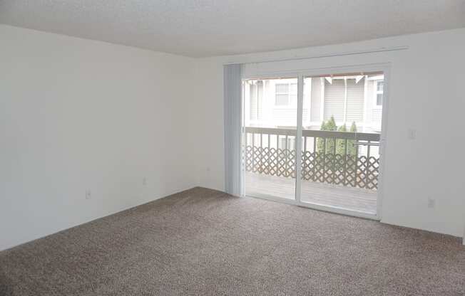 an empty living room with a sliding glass door to a balcony