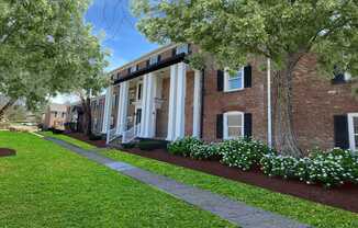 A building with a brick facade and a white trim is surrounded by a well-manicured lawn and trees.