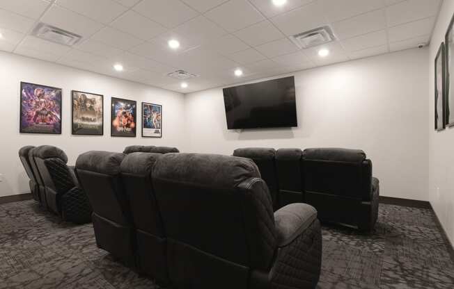 a room with a large screen television and a row of black leather chairs