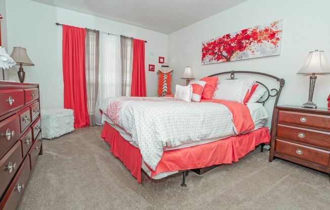 A bedroom with a large bed and red curtains at Laurel Parc apartments in Shreveport, LA.