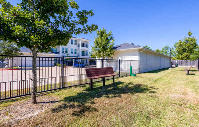 A park with a bench, a tree, and a fence.