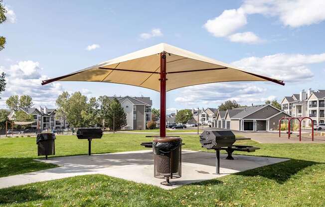 A park with a bench and a trash can under a canopy.