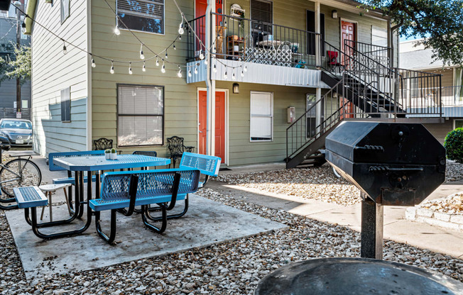 a patio with a table and chairs and a grill in front of a house