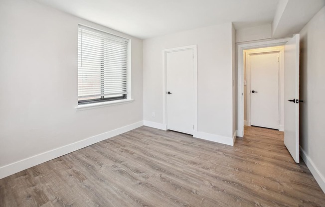 a bedroom with white walls and wood flooring and a window