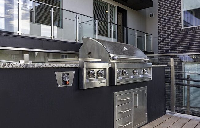 A stainless steel outdoor grill with a side burner and a drawer is on a black countertop.
