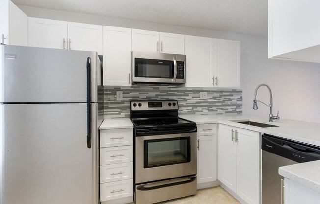 Kitchen with cabinets, sink with vegetable sprayer, tile back splash, stainless steel oven, microwave, and refrigerator, and dishwasher.