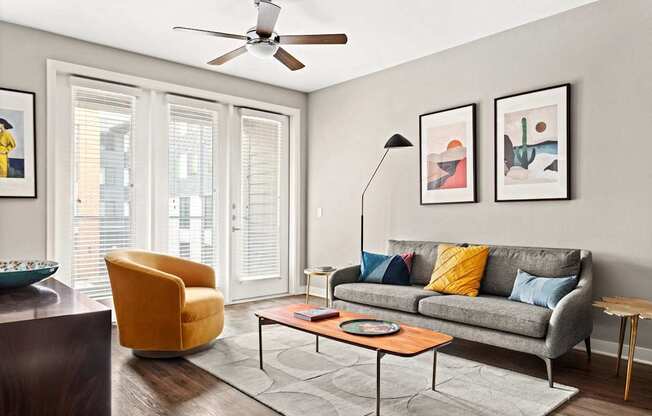 A living room with a grey couch, a yellow chair, a coffee table, and a ceiling fan.