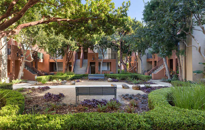 A bench is situated in the middle of a garden with a building in the background.