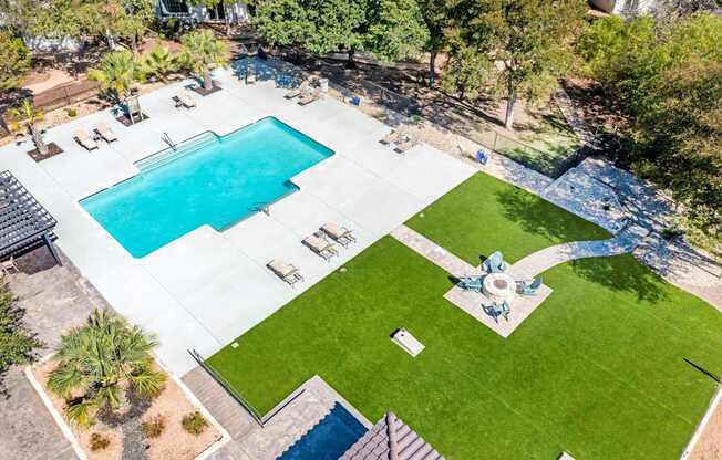 An aerial view of a swimming pool surrounded by a grassy area and trees.
