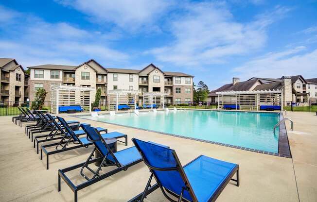 A pool area with sun loungers and apartment buildings in the background.