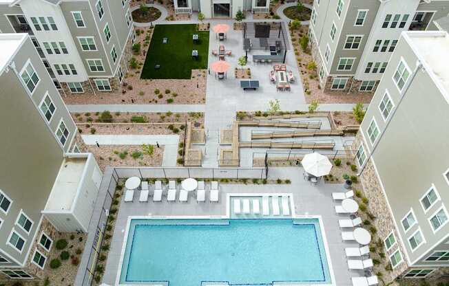 A large swimming pool is surrounded by white lounge chairs and umbrellas.