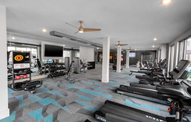 a gym with treadmills and other workout equipment in a building with windows