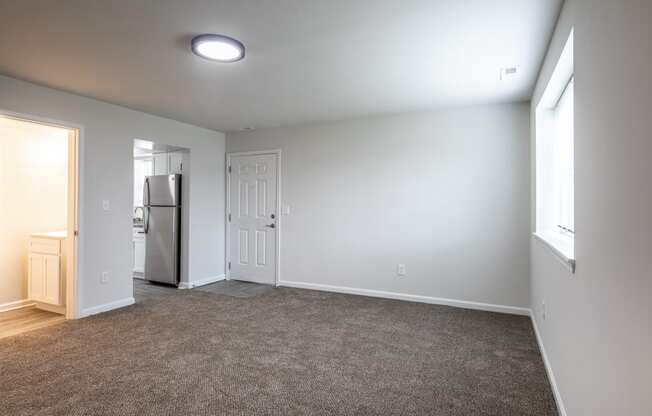 an empty living room with white walls and a door to the kitchen