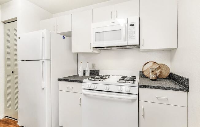Virtually staged kitchen with white appliances, wood flooring, gas stove and white cabinetry