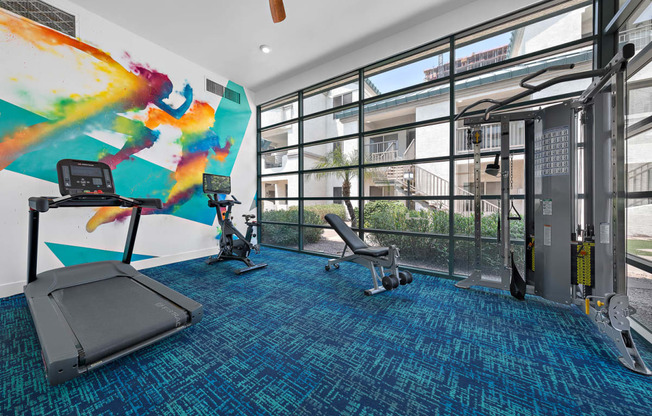 a workout room with floor to ceiling windows and a colorful mural